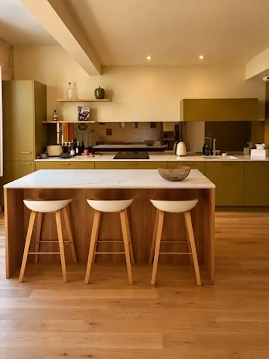 Cuisine vert olive avec îlot en bois et plan clair, sur un parquet en chêne