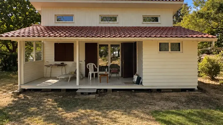 Maison en bois repeinte en blanc cassé, avec sa terrasse couverte, au milieu des pins