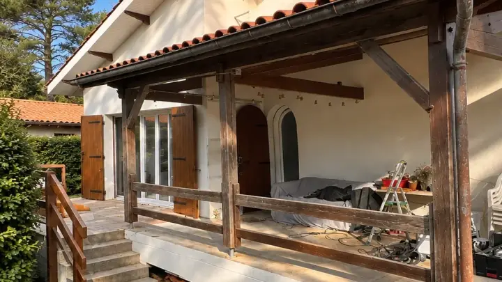 Terrasse couverte avant rénovation : poteaux, poutres et garde-corps en bois grisé